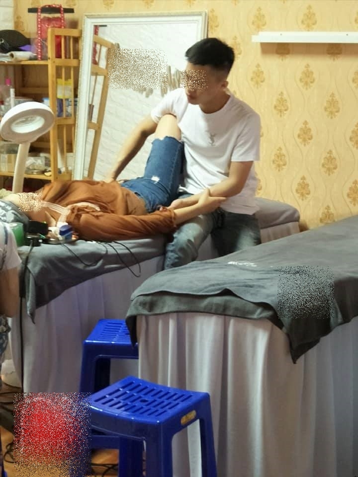 Chàng trai ngồi bên cạnh nắm tay bạn gái trong lúc xăm môi.