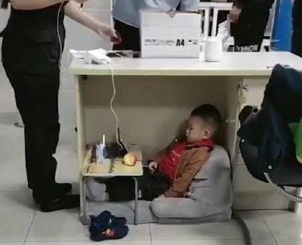 Hình ảnh bé trai ngồi ngoan ngoãn dưới gầm bàn làm việc của mẹ.