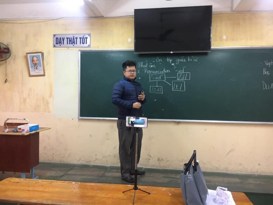 Hình ảnh một thầy giáo đang đứng livestream dạy học trên bục giảng.