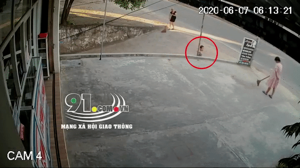 Bé gái đang chơi trước cửa nhà. Gần đó là 2 người phụ nữ đang quét sân.