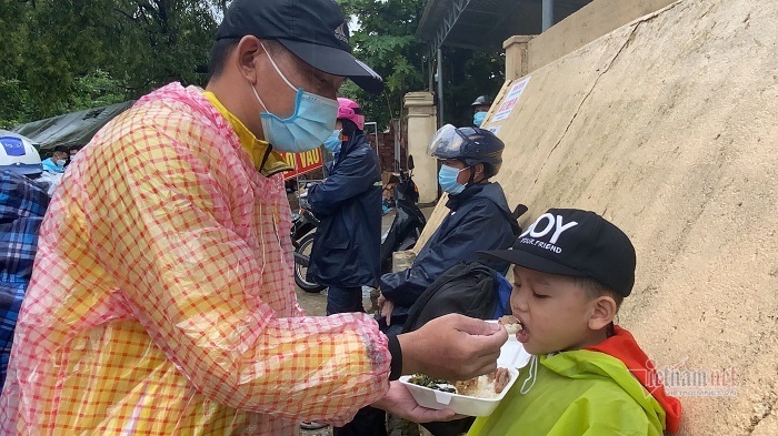 Tranh thủ trời tạnh, người đàn ông cho con ăn vội cơm để tiếp tục hành trình về quê. Ảnh: Quang Thành