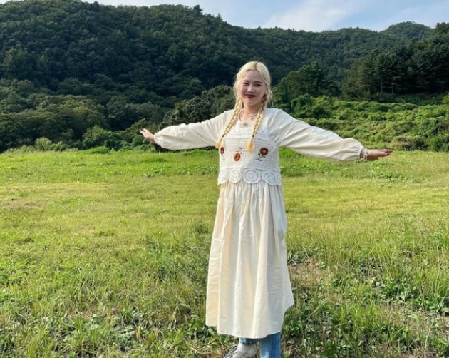 Hyojung (Oh My Girl) diện chiếc váy maxi màu trắng ngà dài đến mắt cá chân được kết hợp với áo len đan móc và xếp lớp cùng quần denim tạo vẻ nữ tính. Áp dụng bản phối này và thả dáng trong khung cảnh bình dị.