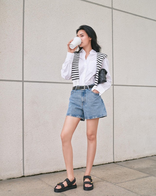 Quần denim short kết hợp rất ăn ý với áo sơ mi trắng. Ninh Dương Lan Ngọc đã tăng sự nổi bật cho bộ đồ bằng cách tô điểm áo len quàng vai và đi sandal đế thô.    