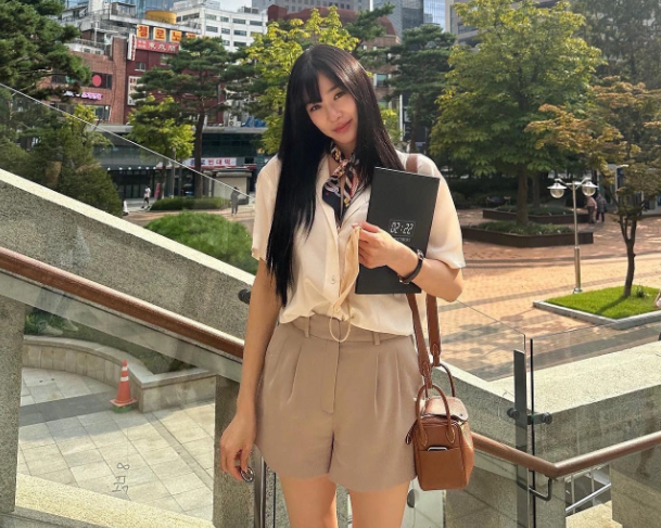 Công thức áo sơ mi trắng và quần short được tạo điểm nhấn cho outfit bằng chiếc khăn quàng họa tiết. Món thời trang này mang đến sự nữ tính, nổi bật cho bộ đồ. Màu sắc nhã nhặn càng giúp cô nàng ghi điểm.