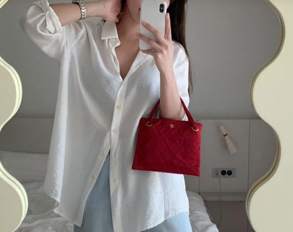 Áo sơ mi trắng và quần jeans xanh nhân đôi sự trẻ trung mà còn mang đến nét thanh lịch. Chiếc túi xách màu đỏ chính là điểm nhấn nổi bật của tổng thể outfit.    