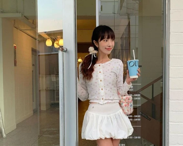 Cô nàng này ưa chuộng công thức chân váy trắng kết hợp cùng áo cardigan mỏng nhẹ in họa tiết hoa nhí, tất dáng dài và giày búp bê nữ tính.    