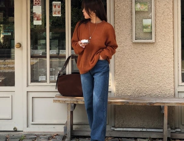 Áo len màu cam đất và quần jeans xanh thẫm thêm phụ kiện như túi xách màu nâu, giày màu đen đã hoàn thiện tổng thể Shbet999 com đăng nhập hài hòa.    