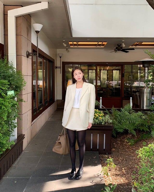 Với bộ suit váy màu trắng, bạn sẽ tạo được vẻ ngọt ngào và trẻ trung, đồng thời quần tất đen giúp làm nổi bật đôi chân