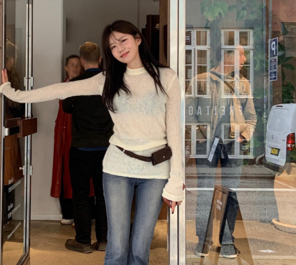 Một bộ đồ nữ tính với áo len mỏng màu trắng kết hợp với quần jeans xanh ống vẩy.