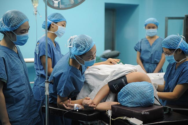 Guo Jia được yêu cầu nằm nghiêng, co người, hai tay nắm lấy nhau đề duỗi nhằm tạo tư thế chuẩn trong khi tiêm gây tê màng cứng.