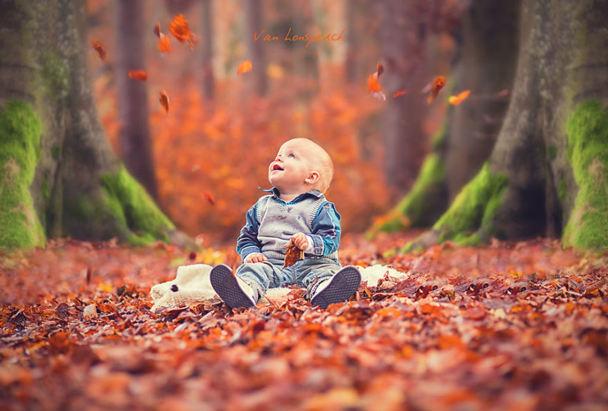Bé trai thích thú vui đùa giữa thảm lá khô.