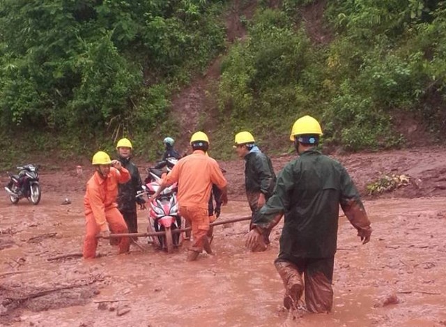 Nhiều người chung sức khiêng xe máy bị sa lầy dưới bùn. Ảnh: Lao động