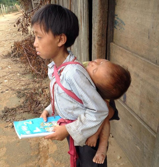 Người anh mặc chiếc áo lấm lem bùn đất, tay đặt trên cuốn sách giáo khoa Tiếng Việt lớp 2. Sau lưng, cậu còn địu thêm em bé khoảng 2 tuổi đang say giấc. Khoảnh khắc do Đàm Thị Lan Anh, sinh năm 1982, chủ tịch câu lạc bộ từ thiện Từ Tâm (TP Vinh, Nghệ An) chụp tại bản Huồi Mới, Tri Lễ, Quế Phong, Nghệ An.