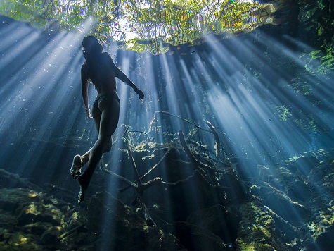 16. Quintana Roo, Mexico: Ánh mặt trời xuyên qua làn nước trong vắt của hố sụt Cristalino ở Quintana Roo khi một cô gái đang bơi lên mặt nước làm cảnh vật càng có vẻ huyền ảo và quyến rũ. Ảnh: Christian Vizl.