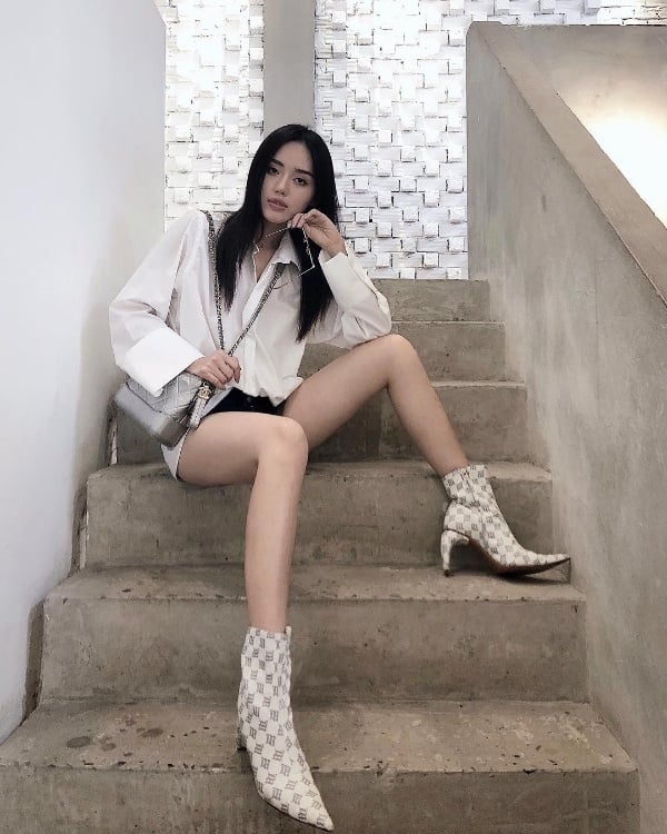 Khánh Linh The Face diện đồ đơn giản nhưng không kém phần trẻ trung cá tính. Cô nàng phối sơ mi trắng  quen thuộc cùng quần short khoe trọn đôi chân thon dài. Những phụ kiện như túi xách và boots da ấn tượng giúp nâng tầm set đồ street style cho cô nàng.    