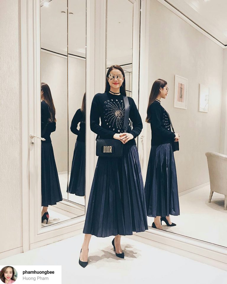 Phạm Hương cũng diện cả cây đen nhưng lại mang đến vẻ điệu đà, thanh lịch. Người đẹp chọn áo len đen họa tiết mặt trời kết hợp cùng chân váy xòe dài xếp li. Phụ kiện quen thuộc của Phạm Hương đó là giày cao gót, túi đeo Dior và kính mắt tráng gương.    