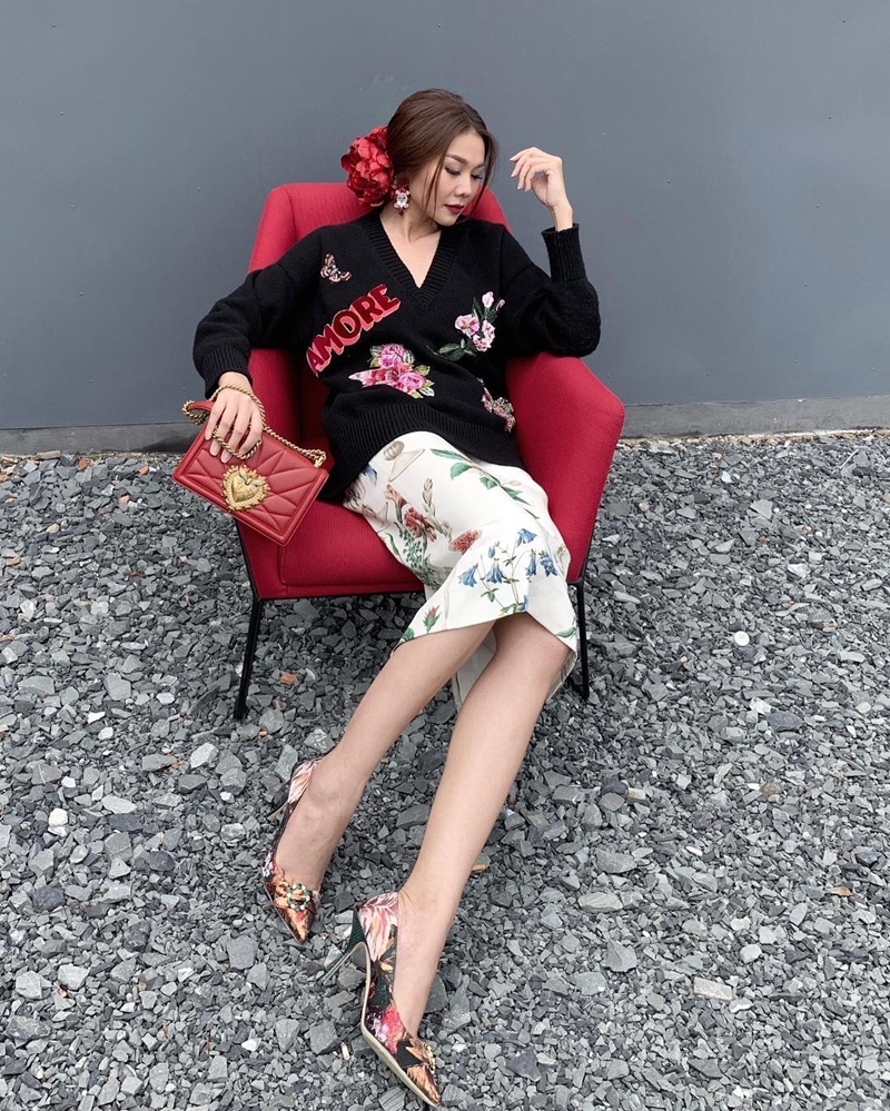 Khác hẳn hình ảnh menswear thường thấy, Thanh Hằng hóa tiểu thư đài các với công thức mix đồ gồm chân váy họa tiết hoa lá và áo len cổ tim dáng rộng. Loạt phụ kiện đắt giá từ Dolce & Gabbana gồm giầy cao gót và túi xách được huấn luyện viên The Face mix&match tài tình, ăn ý.    