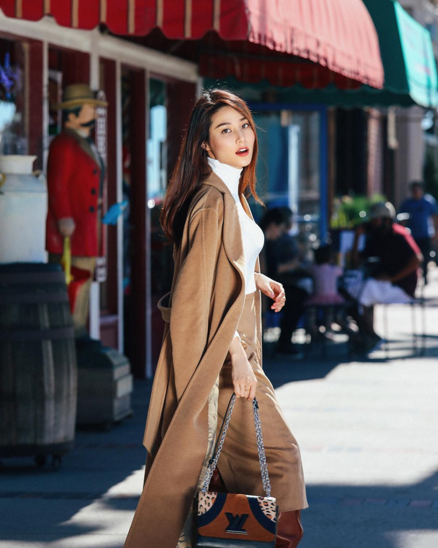Diễm My 9X diện áo cổ lọ bên trong trench coat dáng dài, rất phù hợp với tiết trời se lạnh những ngày đầu đông. Cô nàng xuống phố sành điệu cùng mẫu túi xách phối họa tiết da động vật của Louis Vuitton.