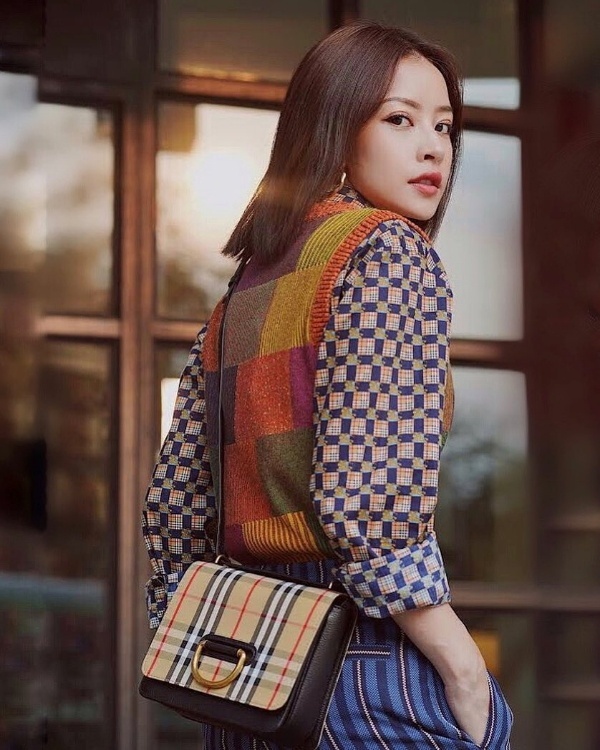  Diện đồ theo xu hướng layer phá cách, Chi Pu mix áo sơ mi họa tiết cùng áo len không tay và quần kẻ sọc. Chiếc túi xách D- ring của Burberry được cô trưng dụng để hoàn thiện set đồ này.    