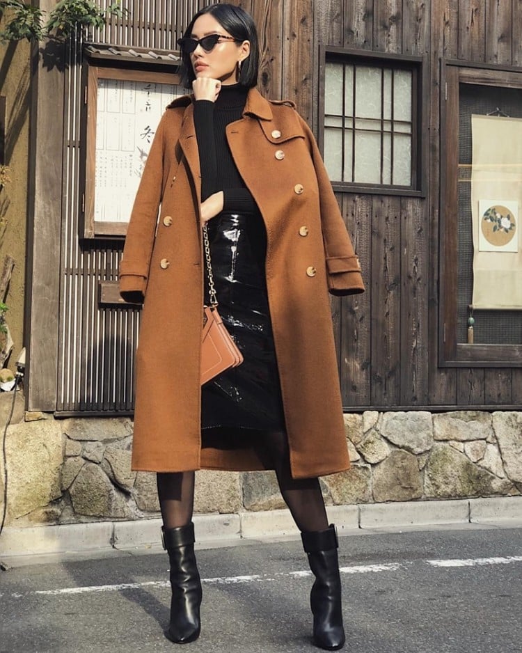 Khánh Linh lựa chọn áo len cổ lọ phối chân váy và boots da tiệp màu đen, thêm áo khoác dáng dài tông nâu trầm  
