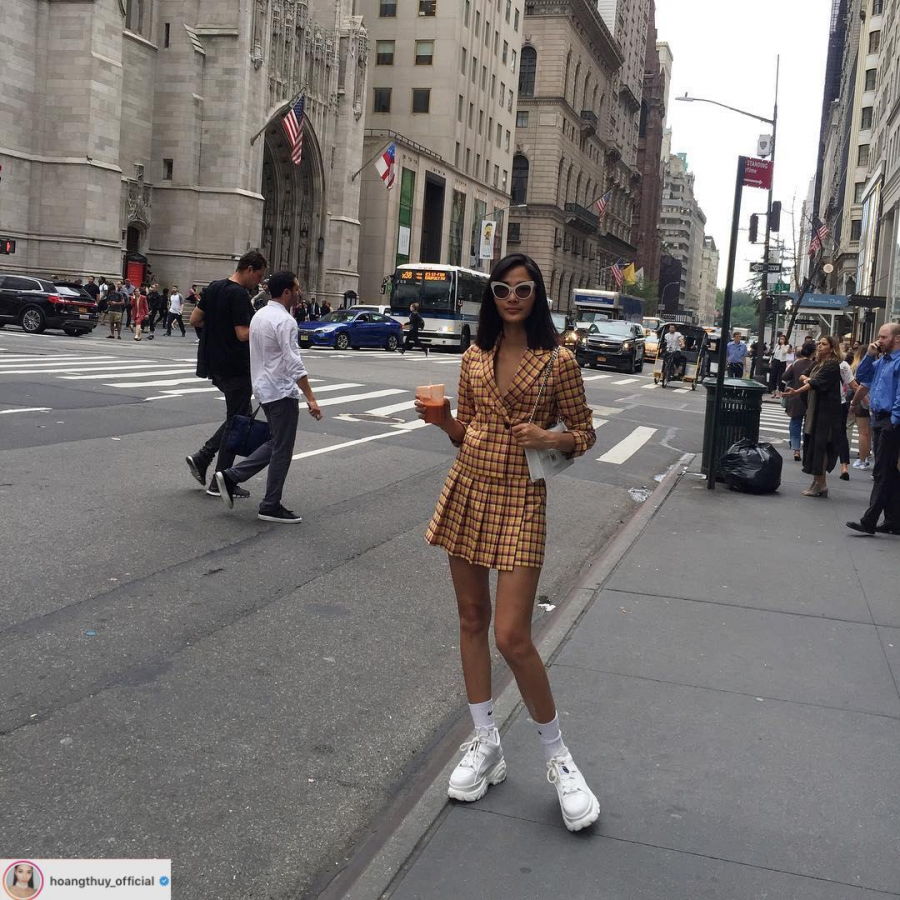 Hoàng Thuỳ khoe dáng trong bộ skirt suit họa tiết kẻ ô. Phụ kiện cùng tông trắng từ kính mắt, túi xách, giày sneakers và tất được kết hợp hài hòa.    