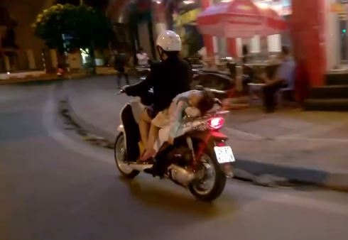 Mẹ SHBET 1000 World Cup bằng 1 tay mặc cho bé gái đang nằm dài sau yên xe ngủ