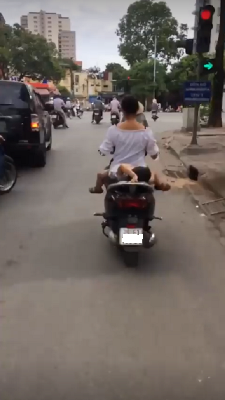 Mẹ vẫn đi dù con nằm vắt vẻo trên yên xe khiến người đi đường hoảng sợ.